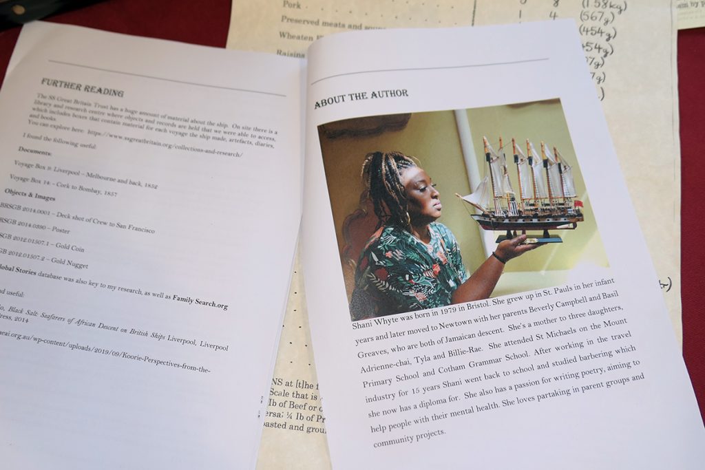 A piece of paper on a table, with a photo of a Black woman holding a ship model. The text on the page around the image says "About the author", who is Shani Whyte.