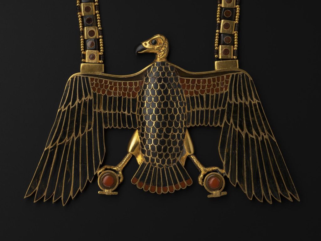 Shining, very new-looking reproduction of a brass vulture with its wings spread like a Roman eagle. The vulture's feathers are black, with red orbs at its feet. 