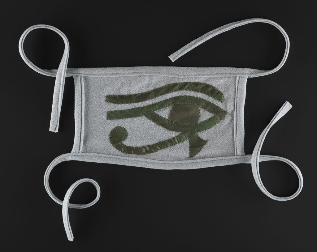 Rectangular Covid-19 face mask with four grey straps on a black background. The mask is light grey, with a green Eye of Horus in the middle.