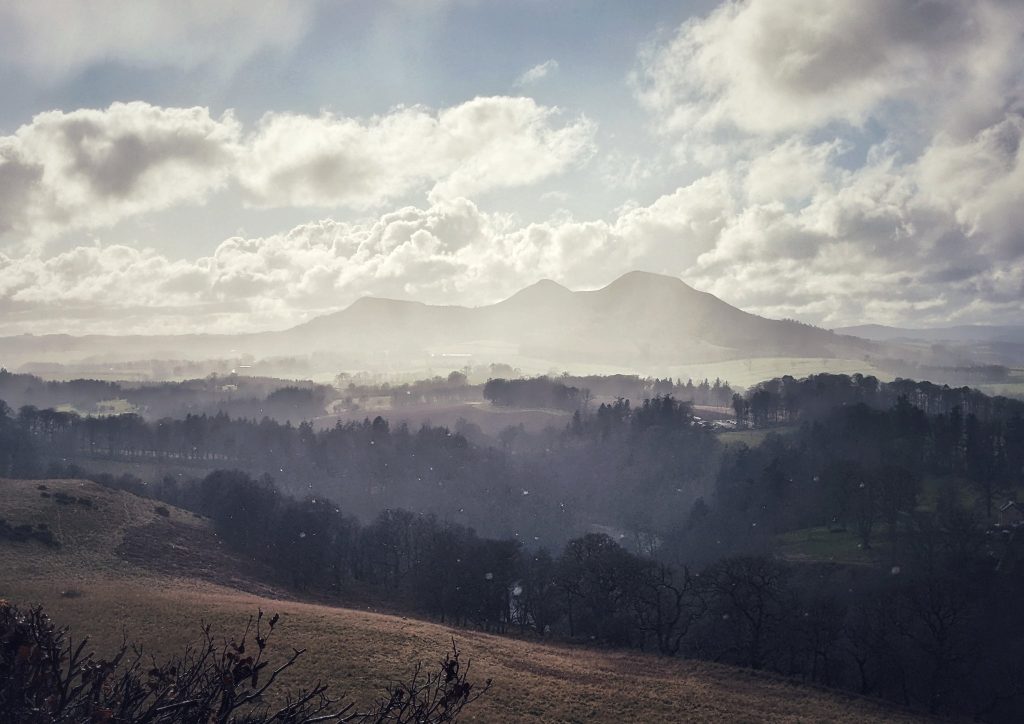 A painting-like image of the Eildon Hills in the distance from Scott's View. Drops of rain fall as the sun peeks out, shrouded the Eildons in a shining mist. A Romantic view if ever there was one!