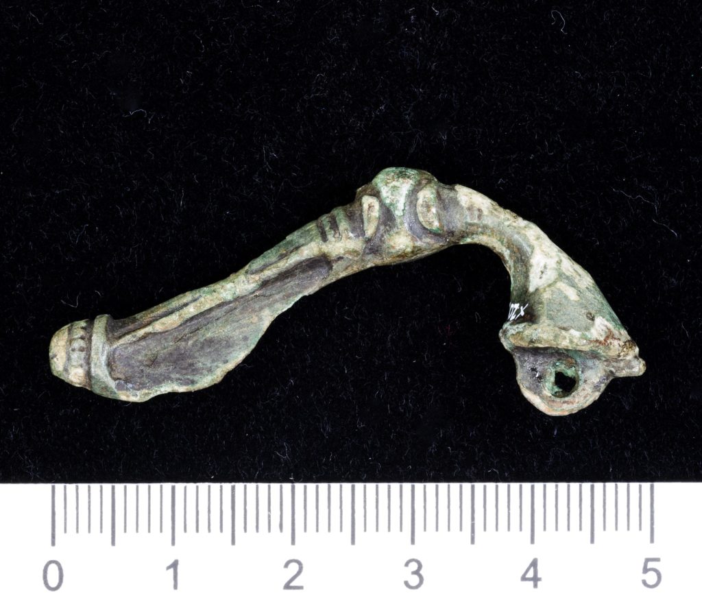 A small brooch in the shape of a curved trumpet against a black background, with a measuring tape below indicating a length of 5cm.