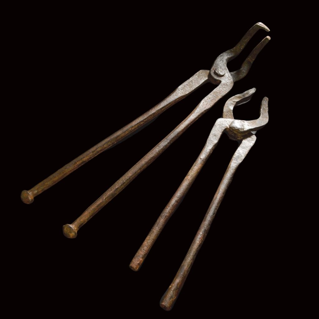 A pair of metal tongs pointing up and to the right against a black background. They look exactly like tongs today, although they are 2,000 years old!