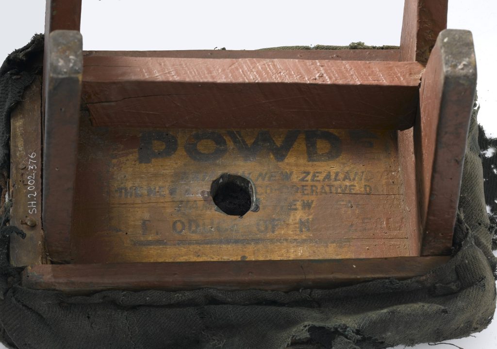 Closeup of the underside of a tiny wooden stool, where the painted words 'POWDER', 'New Zealand', and 'Product of' are visible.