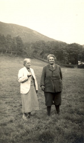 Black and white photo of May in a skirt and jacket and Mary in trousers and a coat.