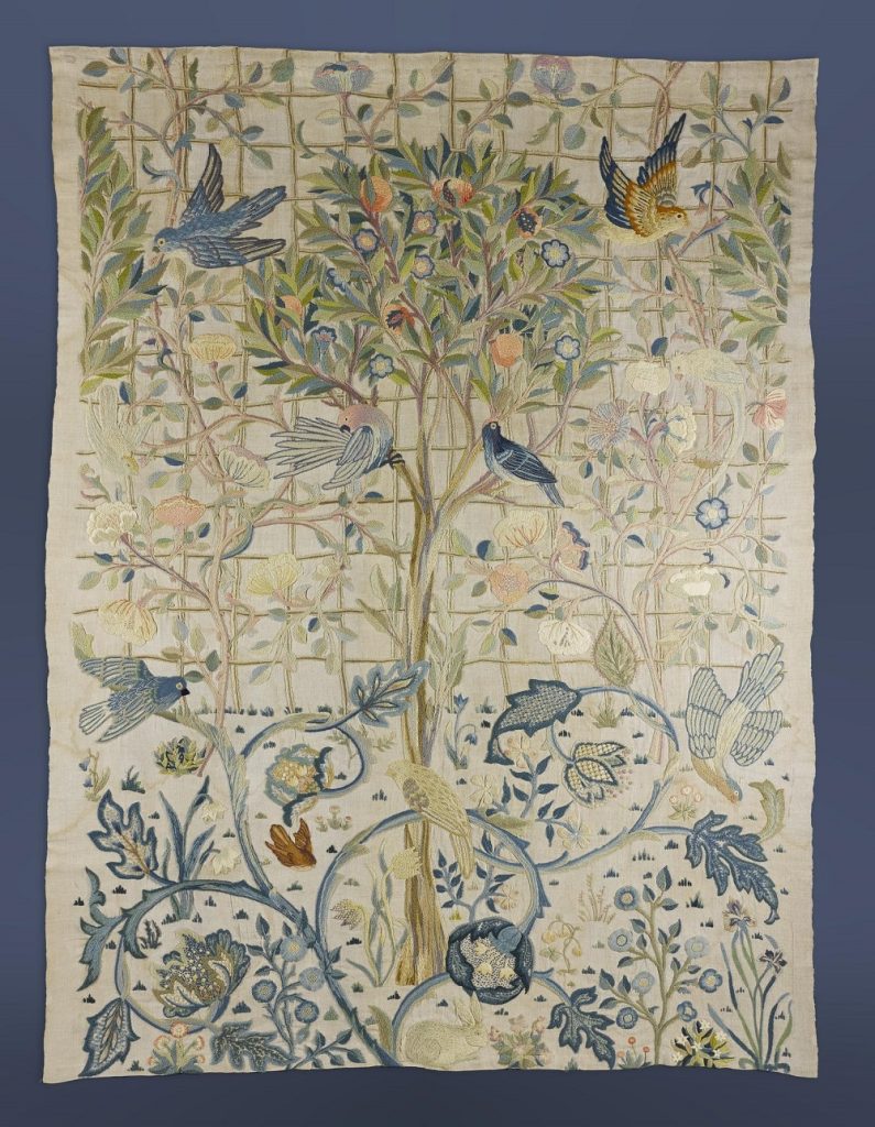 An elaborate, rectangular embroidered fabric decorated with swirling vines, colourful birds in flight, and a thin fruit-bearing tree in the centre.