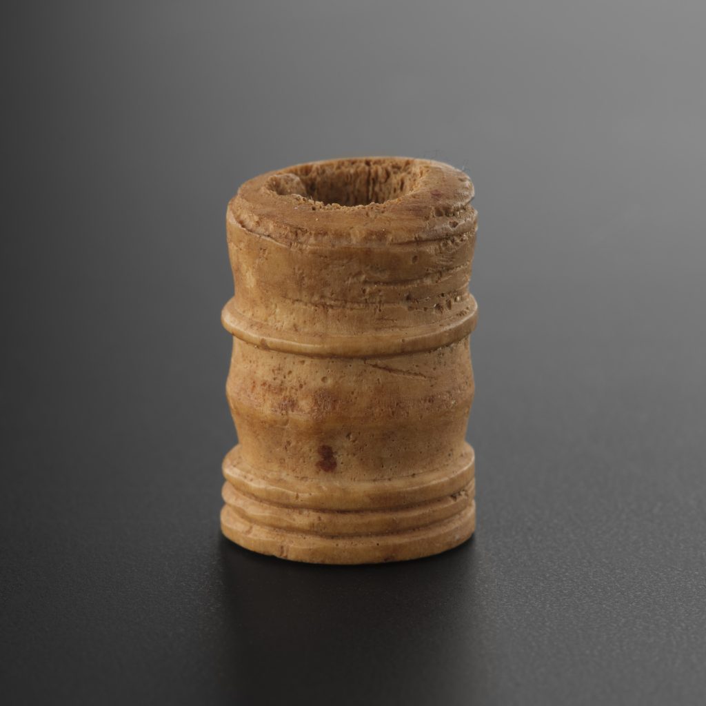 Closeup of a small, cylindrical gaming piece, a little like the lower section of a chess pawn, upright against a grey background. The piece is orange-yellow, and has a hole burrowed into it from the top down.