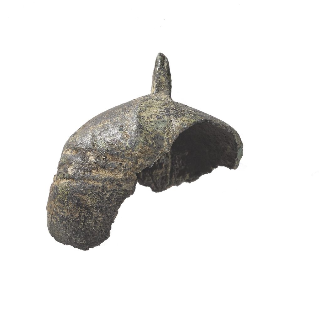 Fragment of a metal bell, perhaps one third of the whole object, with a tiny point atop it against a white background.