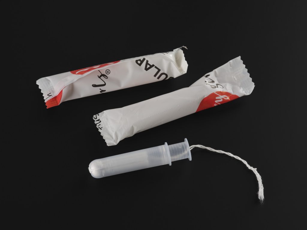 A small, clear applicator tampon with two white and red packages, one opened and one closed, above it on a black background.