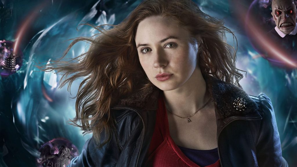Closeup of Karen Gillan, a red-haired young woman, as Amy Pond seen from shoulders up. Behind her is an abstract, swirling blue background meant to to evoke space travel and, each in small purple bubbles, three faces of Doctor Who villains including a Dalek.