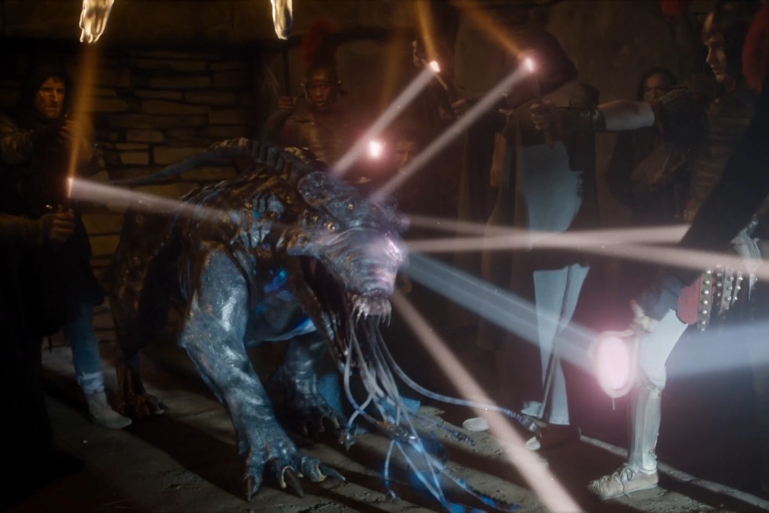 A creature on all fours resembling a hybrid of a wolf, dolphin, lion, and alien from Predator with several soldiers standing around it. Multiple beams of light are directed at the beast.