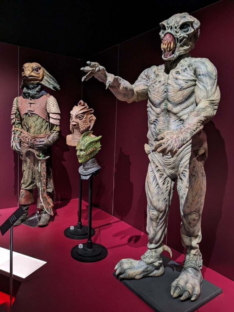 Costumes for Doctor Who characters including three types of lizard-like Silurian and a monstrous, muscular humanoid 'dreg' with one claw extended forward. 