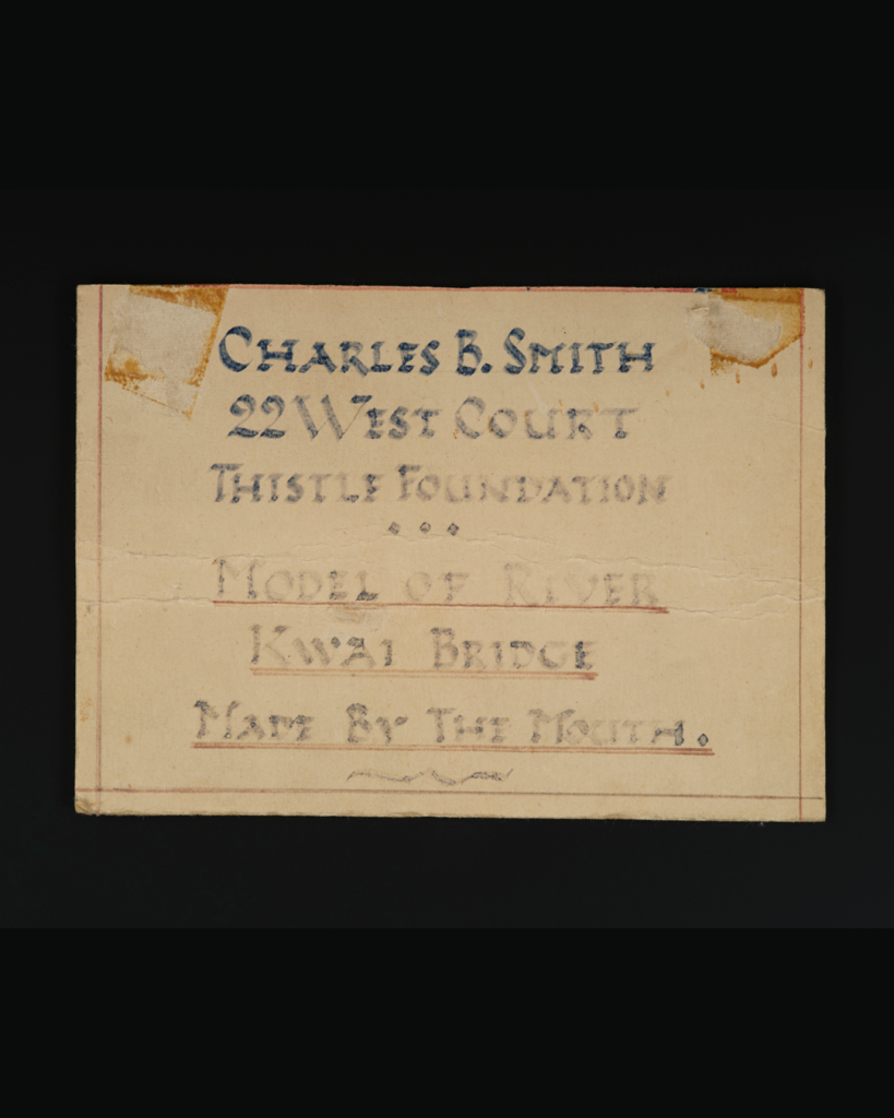 Label which reads “Charles B. Smith, 22 West Court, Thistle Foundation, Model of River Kwai Bridge, Made by Mouth.”