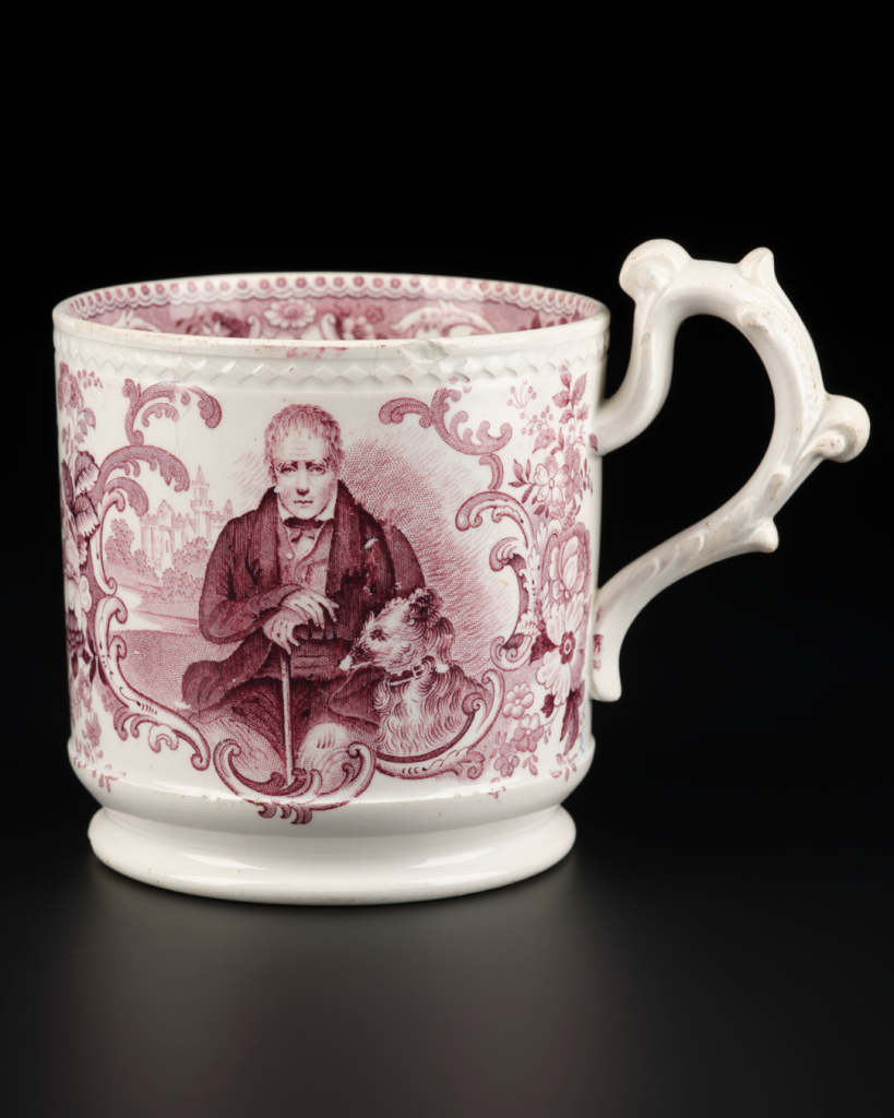 Cream-coloured mug decorated with a maroon transfer print showing a portrait of a seated Walter Scott wearing a suit, waistcoat, shirt and bowtie and holding a walking stick in front of him.