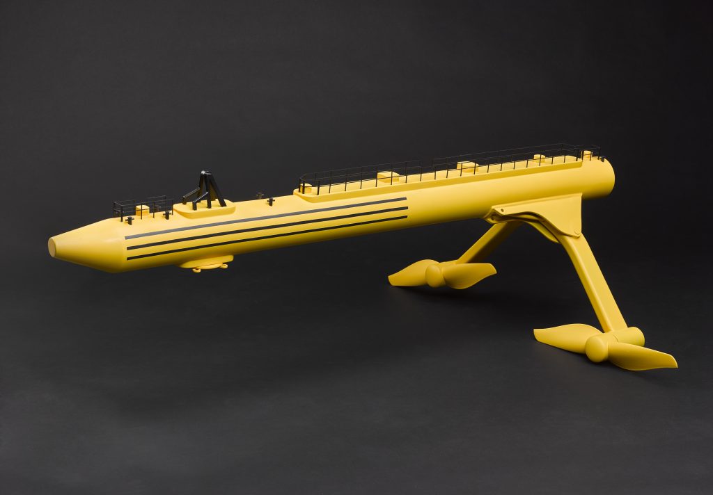 A yellow model of a tidal energy convertor. A long cylindrical generator with two legs with propellers at the end.